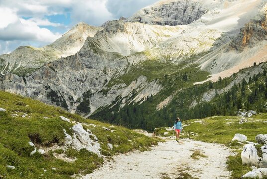 Female hiker with backpack walking dirt trail green alpine meadow majestic mountain peaks background Malga Rossalm Dolomites Italy summer adventure travel lifestyle