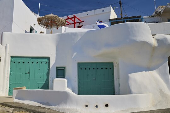 White, cubist building with green doors and shady parasol in a Mediterranean atmosphere, syrmata, boat garages, boathouse, boathouses, beach house, Goupa, Goypa, Goupa Kara, Kimolos, Cyclades, Greek Islands, Greece