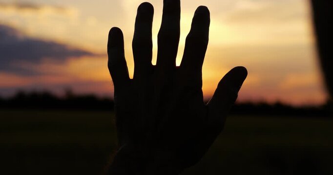 Silhouette of male hand against colorful sunset sky inspires dreams, creativity and limitless possibilities. Warm evening light creates motivational and artistic visual concept. Hand silhouette