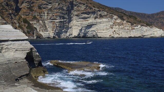 Whipped waves break on limestone rocks with boat in the blue sea, white volcanic strata, bizarre white rocks in the sea, Little Sarakiniko, Kioni Beach, Kioni, Kimolos Island, Cyclades, Greek Islands, Greece