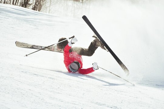 Skier fall down hit head painfully on hard groomed piste with snow swirls on ski resort slope. Sports Injury young skier in professional sports concept