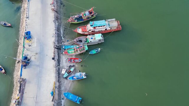 Fishing Boats at the Pier: A serene aerial view captures a collection of colorful fishing boats docked alongside a weathered pier, with calm, jade-green water reflecting the tranquil scene.