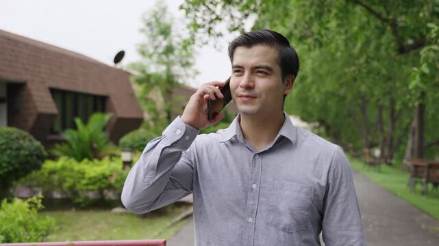 Portrait of happy handsome Caucasian businessman in a shirt holding and using a smartphone while walking on the street outdoors in a public park. A young white male uses a mobile phone in a village. 
