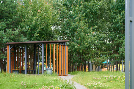 Modern wooden pavilion surrounded by lush green trees in a public park