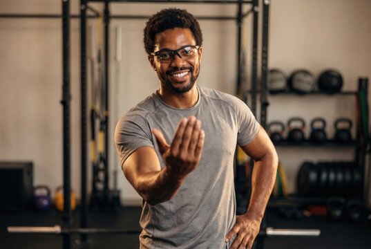 Smiling man in glasses making a beckoning gesture at a gym