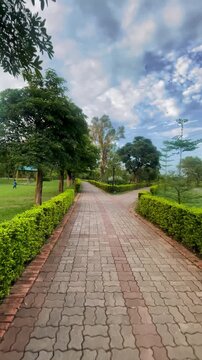 Walking Through a Scenic Green Park Pathway with Lush Trees and Beautiful Landscape &ndash; Peaceful Nature Walk, Brick Track, Garden Trail and Outdoor Environment in Daylight
