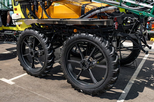 Narrow row crop wheels and chassis on self propelled field sprayer. Agricultural crop protection machine detail featuring high clearance spoke wheels, yellow tank, and boom folding system.
