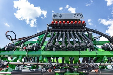 Section control valve manifold on agricultural boom sprayer. Field crop protection machinery detail featuring electric valve actuators with red caps, hydraulic hoses, and green metal frame. © NastyaPhoto