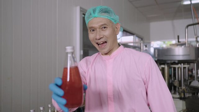 Professional Asian inspector in uniform of food and drink factory holding a juice beverage bottle promoting and advertising healthy nutritional benefits in production line at a manufacturing industry.