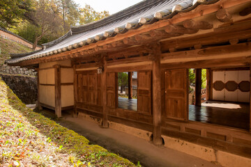 Obraz premium Exterior View of Traditional Korean Hanok House Featuring Wooden Structure, Veranda, and Tiled Roof Set Along a Slope
