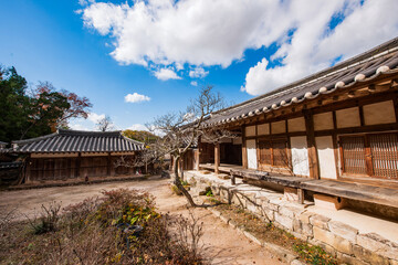 Obraz premium Traditional Korean Hanok House Featuring Wooden Structure, Stone Foundation, and Tiled Roof Set Against a Dynamic Blue Sky and White Clouds