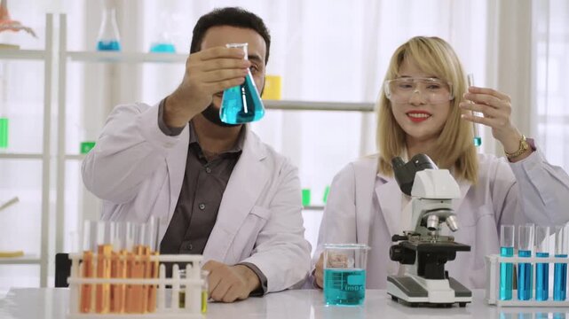 Male and female scientists and researchers in lab coats with microscope are conducting chemistry experiments with liquid in test tubes and beakers in laboratory. Two chemistry experts working in lab. 
