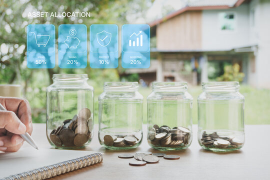Personal financial income allocation planning with glass jars, coins, financial budgeting categories, spending, saving, protection and investing strategy on wooden desk with natural home background