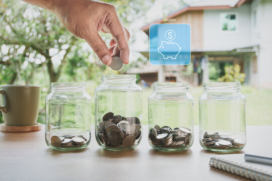 Building savings habit by depositing coins into glass jar for personal financial planning, emergency savings, budget management and long-term financial security with natural home workspace background