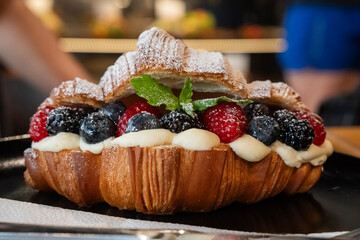 świeży croissant posypany cukrem pudrem z borówkami, malinami, liśćmi mięty oraz bitą śmietaną. © siwyk