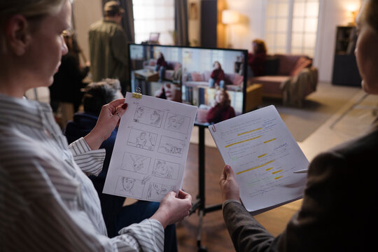 Woman reviewing storyboard and script with crew on film set indoors