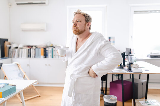 Businessman wearing bathrobe in office holding cup