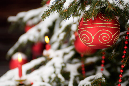 Red bauble and lit candles on snow covered Christmas tree outdoors