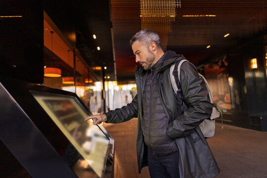 Man using touchscreen in urban outdoor setting with backpack