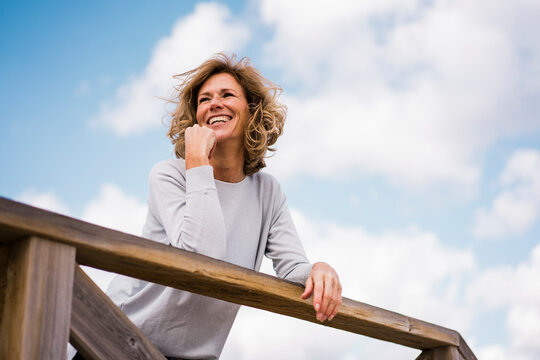 Happy mature woman leaning on railing under cloudy sky