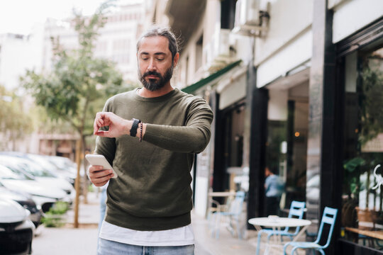 Man holding smart phone checking time on wristwatch