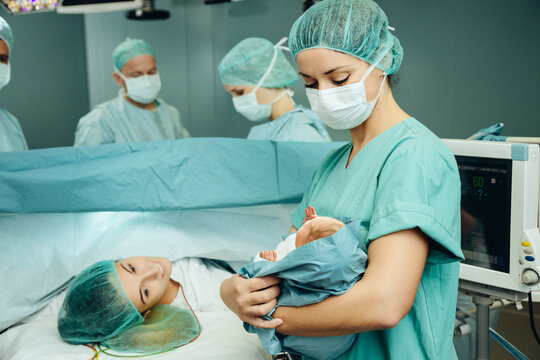 Operating room nurse showing newborn to mother