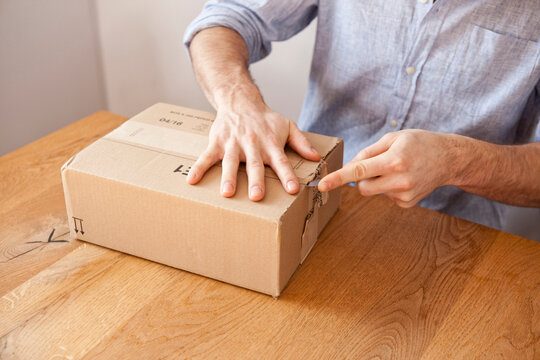 Man's hand unpacking cardboard box with a knife