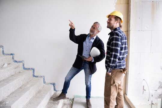 Male architect guiding construction worker while standing on steps in renovating house