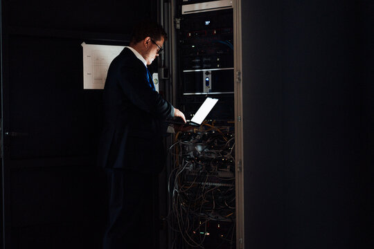 Businessman works on a laptop at the dark office network cabinet