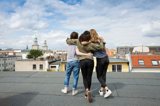 Germany, Berlin, back view of three teenage girls standing arm in arm on roof top