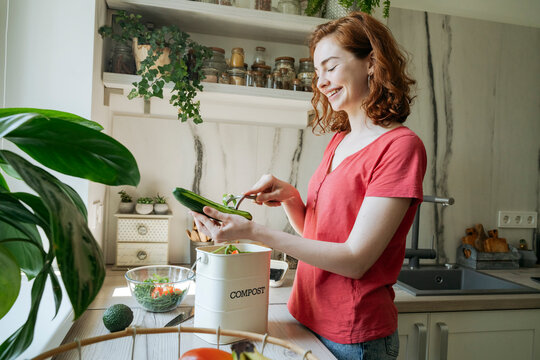Happy woman peeling cucumber in kitchen at home