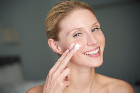 Portrait of happy beautiful woman applying cream on her cheek