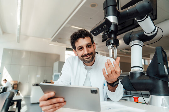 Scientist holding digital tablet with robotic arm in laboratory