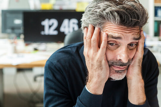 Mature man sitting in office with head in hands
