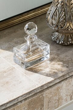 Antique crystal perfume bottle with faceted stopper on travertine vanity shelf illuminated by soft morning light from the left