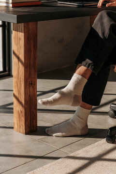 Closeup of a man's feet in white cotton socks resting against a reclaimed wood desk leg in a stylish industrial home office setting