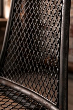 Closeup of black wire-frame chair mesh texture in an industrial loft home office, warm afternoon light highlighting the intricate weave