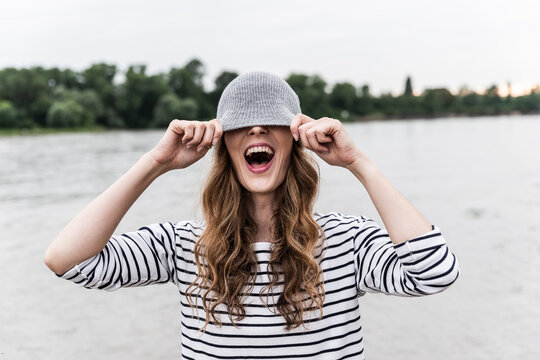 Laughing woman playing with wooly hat at a river