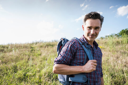 Smiling hiker with backpack standing in a sunny grassy field