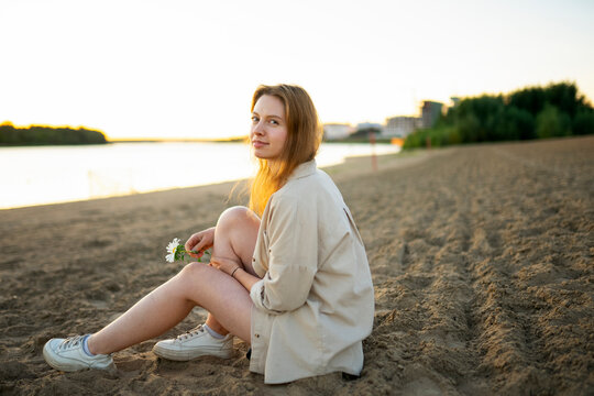 Happy girl sitting on the sand at the river beach during sunset