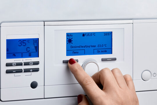 Woman adjusting control panel of heating boiler at home
