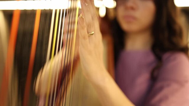 Artistic close-up shot of a woman delicately playing harp strings, her hand in focus with warm bokeh lighting. Captures elegant motion, musical concentration, and vibrant texture detail.