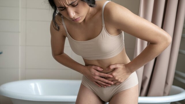 Young woman in beige underwear holds her pelvic area. Female suffers from urinary tract pain or infection. Healthcare concept for women health issues.