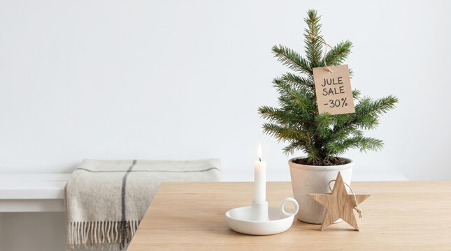 Small potted Christmas tree with holiday sale tag on wooden table. Candle and wooden star decoration. Discount concept for winter holiday shopping. Festive home interior decoration in house.