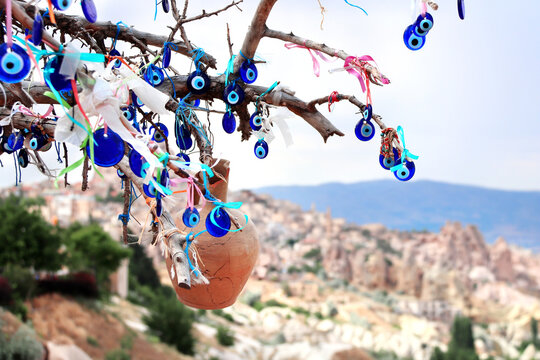Traditional Turkish Nazar amulets, known as evil eye charms, hang in abundance from the branches of a wishing tree against the scenic backdrop of Pigeon Valley in Cappadocia, Anatolia, Turkey