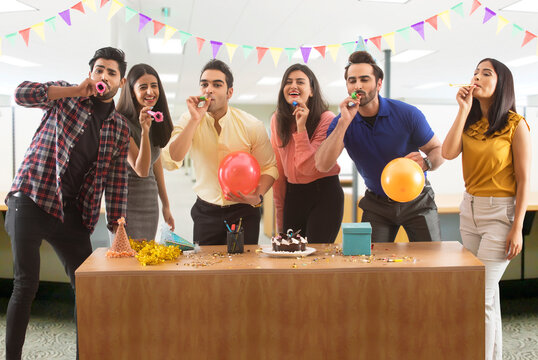 Group of colleagues blowing party hooters during a celebration in office. 