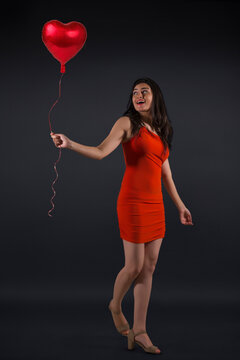 Beautiful woman in a party outfit holding a heart shaped balloon. 
