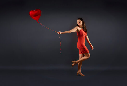 Beautiful woman in a party outfit posing with a heart shaped balloon. 