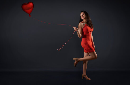 Beautiful woman in a party outfit posing with a heart shaped balloon. 