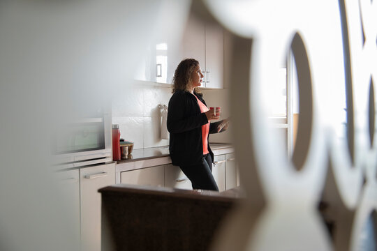 Woman drinking coffee while being lost in her thoughts in the kitchen at home. 